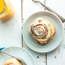 two plates with overnight cinnamon rolls, a fork, and orange juice