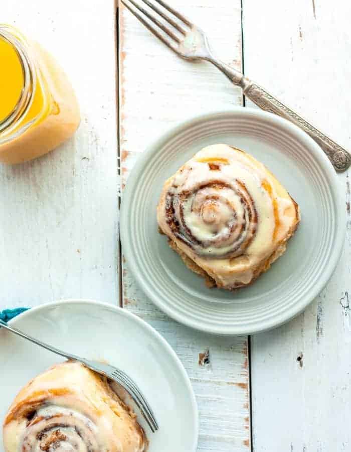 two plates with overnight cinnamon rolls, a fork, and orange juice
