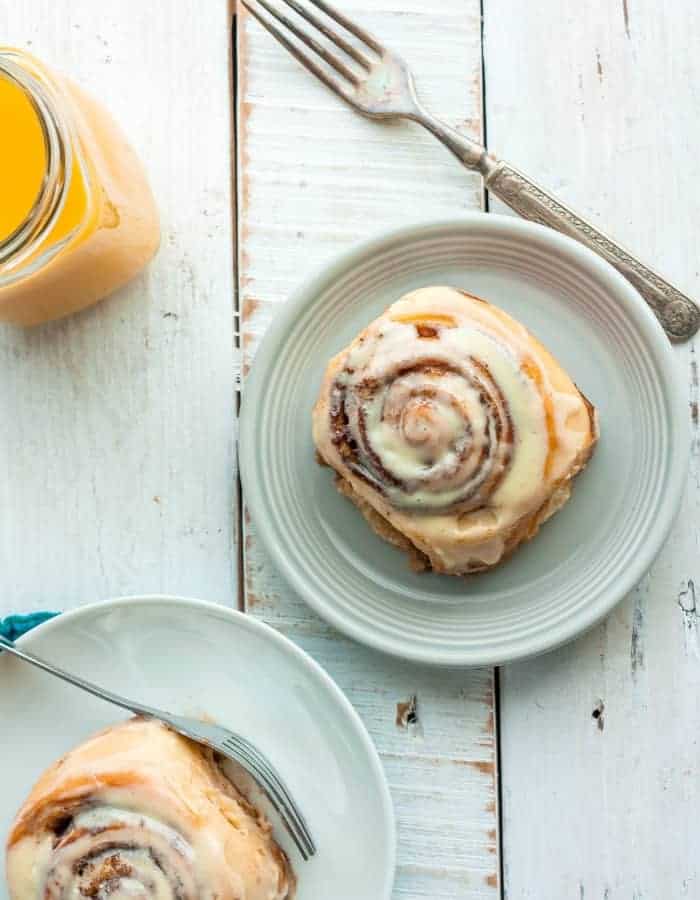 two plates of overnight cinnamon rolls with a fork and glass of orange juice
