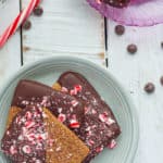 A plate of peppermint bark graham crackers with candy canes and chocolate chips on a white board