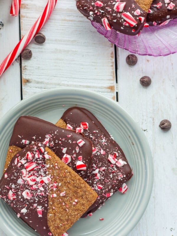 A plate of peppermint bark graham crackers with candy canes and chocolate chips on a white board