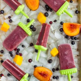 red healthy tea popsicles for sore throats and fruit on a tray of ice cubes