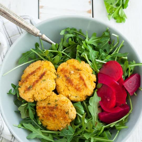 a bowl of arugula with three cauliflower patties and pickled vegetables