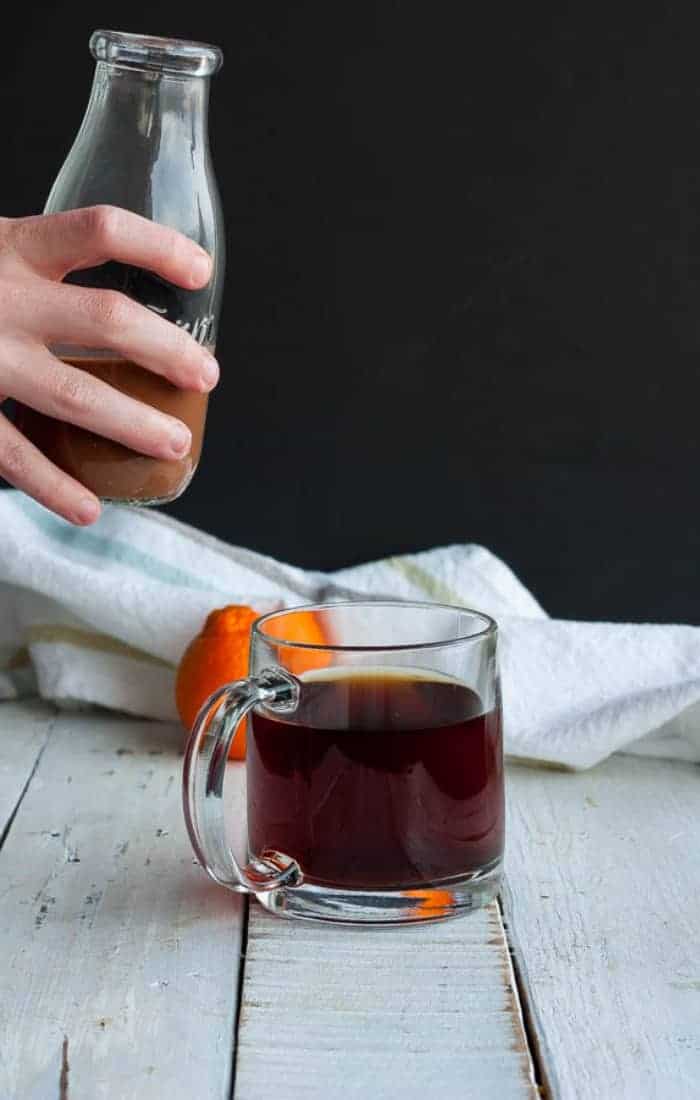 a glass bottle in a hand with coconut coffee creamer and a mug of coffee