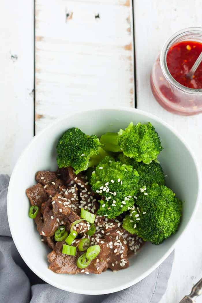 An overhead photo of a bowl of paleo beef and broccoli with sesame seeds and hot sauce