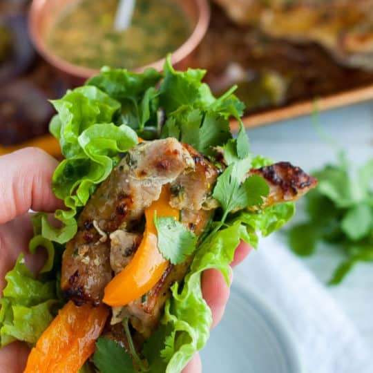 A hand holding a lettuce wrapped pork fajita with peppers and onions