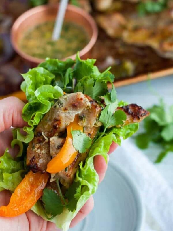 A hand holding a lettuce wrapped pork fajita with peppers and onions