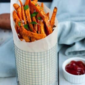 A container of spicy sweet potato fries with parsley and ketchup