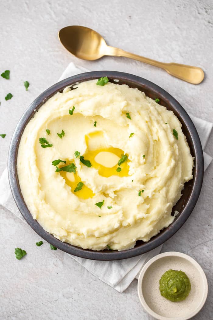 an overhead shot of mashed potatoes with wasabi and a gold spoon on a grey board