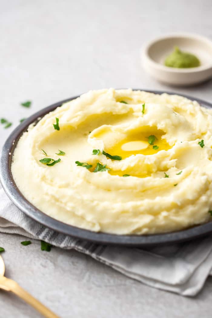 A grey bowl with mashed potatoes topped with butter and herbs, and a small dish of wasabi in the background