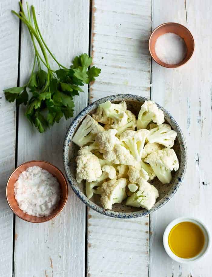 a bowl of cauliflower, dish of olive oil, and other ingredients for air fryer cauliflower