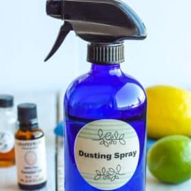 a blue bottle of homemade dusting spray with essential oils and a lemon and lime