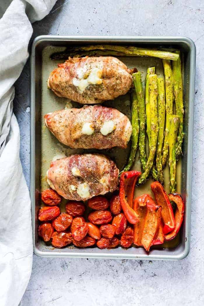 healthy stuffed chicken breasts with asparagus and tomatoes on a sheetpan