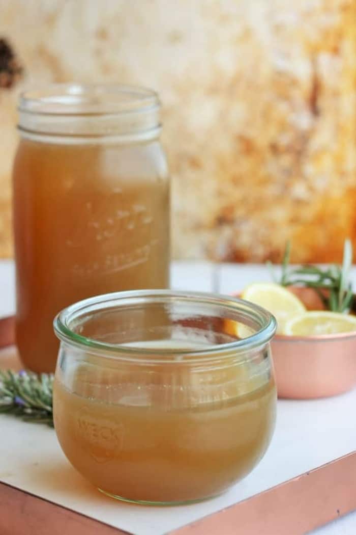 two jars of homemad chicken bone broth on a tray with lemons and rosemary.
