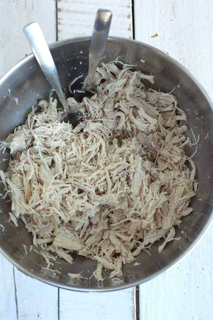 A bowl with shredded instant pot chicken and two forks