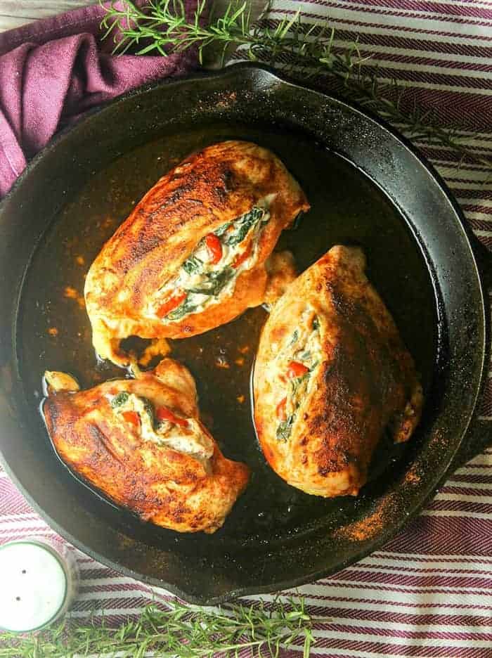 cheese stuffed chicken breasts in a cast iron skillet with rosemary