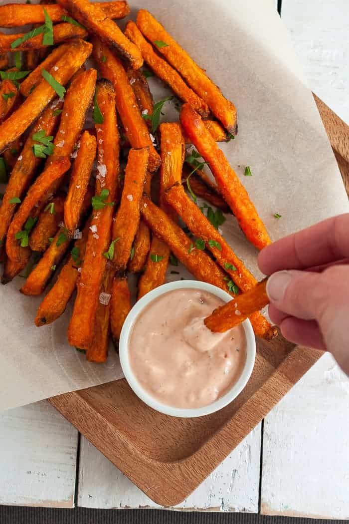 a hand dipping a fry into sweet potato fries aioli