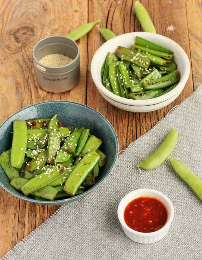 two bowls of sesame snow peas with sesame seeds and hot sauce