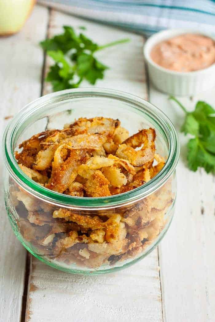 a bowl of crispy fried onions with parsley and dipping sauce