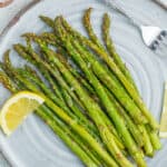 roasted air fryer asparagus on a grey plate with lemon wedges