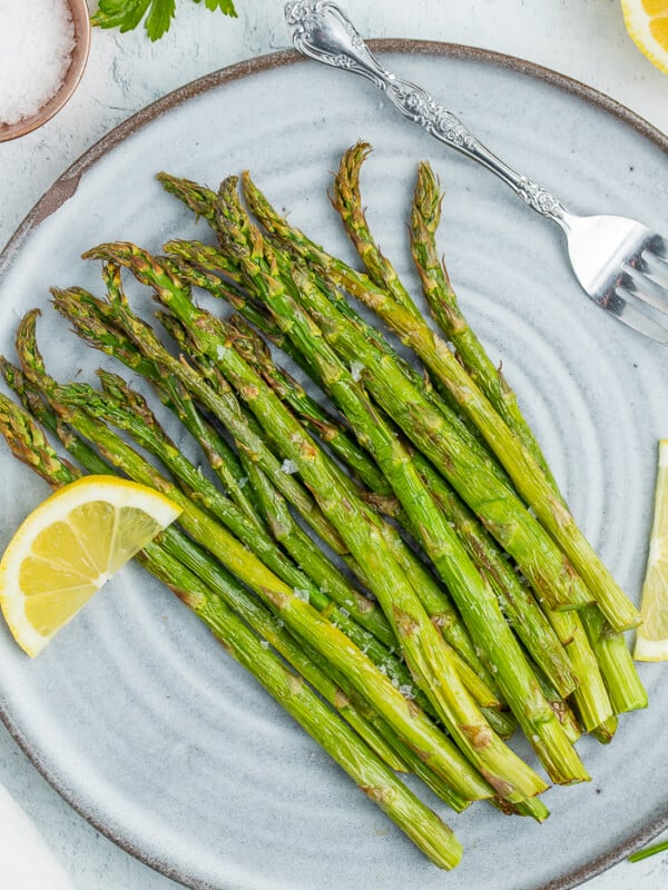 roasted air fryer asparagus on a grey plate with lemon wedges