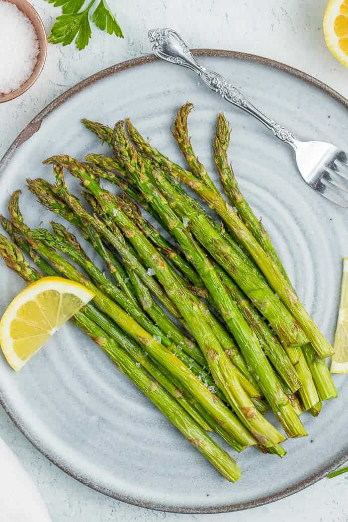 roasted air fryer asparagus on a grey plate with lemon wedges