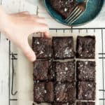 a hand reaching for a brownie on a baking rack
