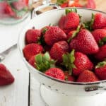 A strainer full of fresh strawberries and a cutting board