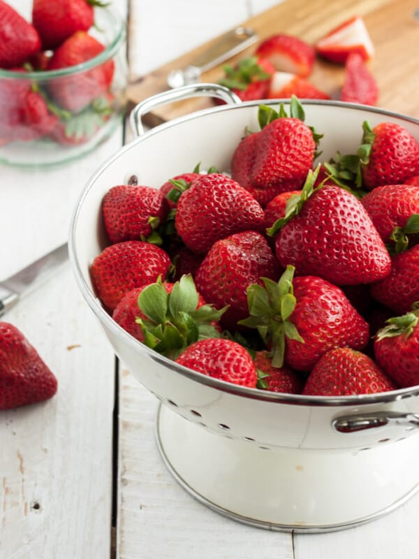 A strainer full of fresh strawberries and a cutting board