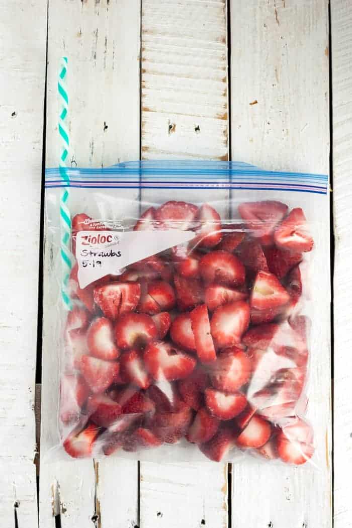 A plastic bag full of strawberries with a straw sticking out