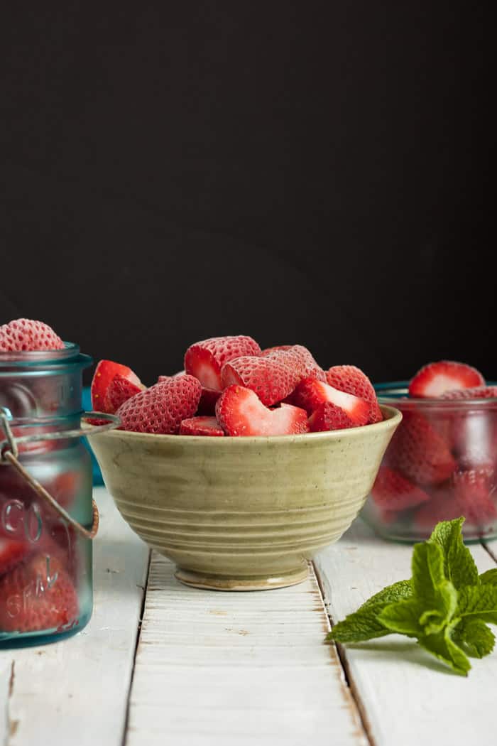 a bowl and two canning jars with frozen strawberries