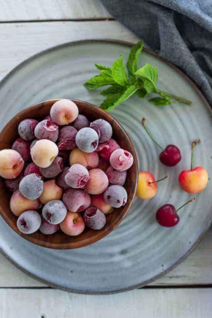 a bowl of frozen cherries on a grey plate with sprigs of mint