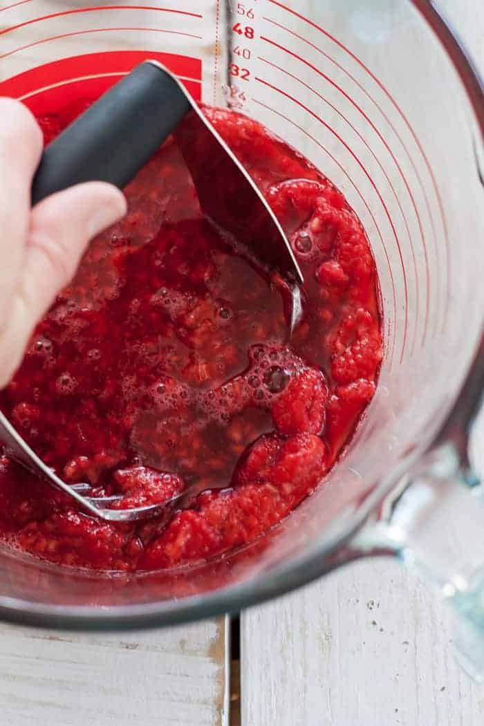 a pastry cutter mashing raspberries for raspberry freezer jam