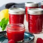 4 jars of raspberry freezer jam on a white board with mint and a lemon
