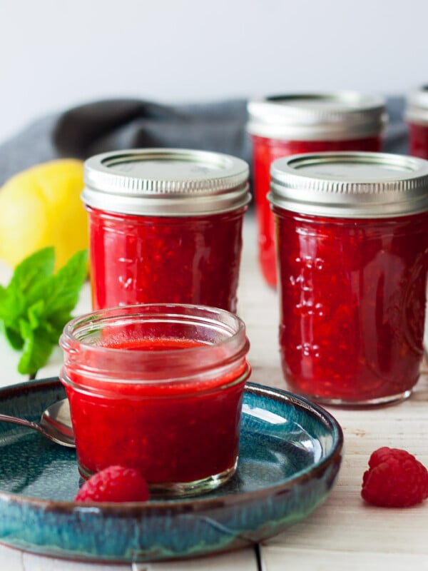 4 jars of raspberry freezer jam on a white board with mint and a lemon