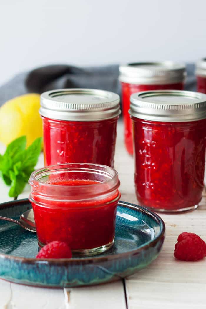 4 jars of raspberry freezer jam on a white board with mint and a lemon