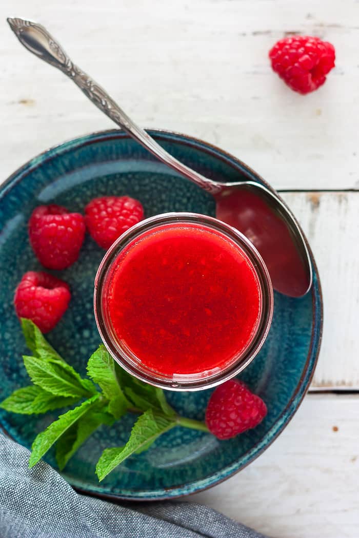 a canning jar of homemade raspberry jam on a blue plate with mint and a spoon