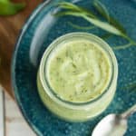 a jar of avocado ranch on a blue plate with herbs and a spoon