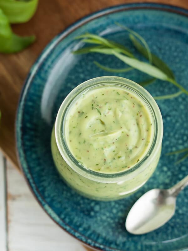 a jar of avocado ranch on a blue plate with herbs and a spoon