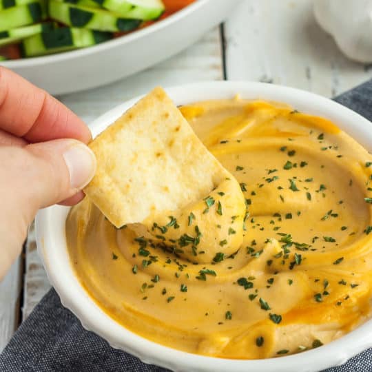a pita chip being dipped into a bowl of buffalo hummus