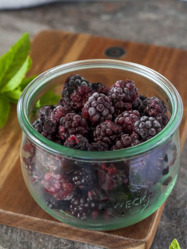 a bowl of frozen blackberries with a sprig of mint