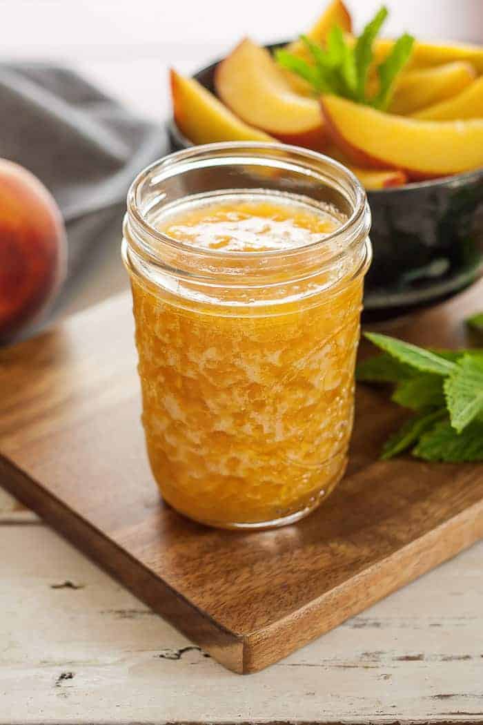 a jar of peach freezer jam on a cutting board with mint and fresh peaches