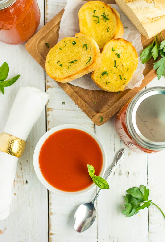 a bowl of tomato soup with canning jars and garlic bread on a plate