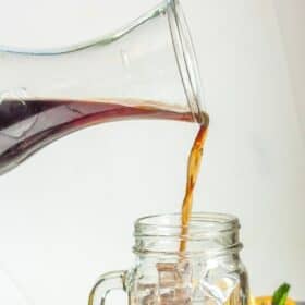 a glass pitcher pouring iced tea into a glass of ice