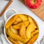 cinnamon apples in a white bowl with an apple and cinnamon stick