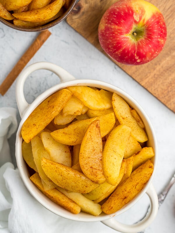 cinnamon apples in a white bowl with an apple and cinnamon stick