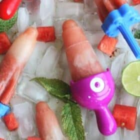 Homemade watermelon popsicles on a tray of ice with lime and mint