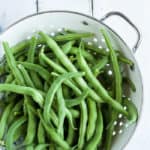 a strainer of green beans on a white board