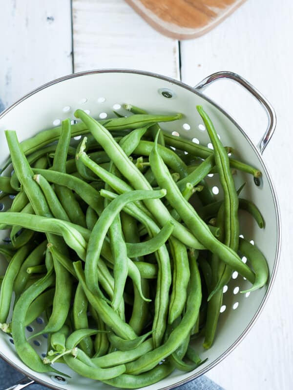 a strainer of green beans on a white board