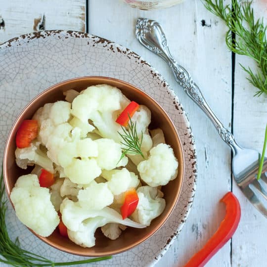 a bowl of pickled cauliflower with red peppers and dill on a white board
